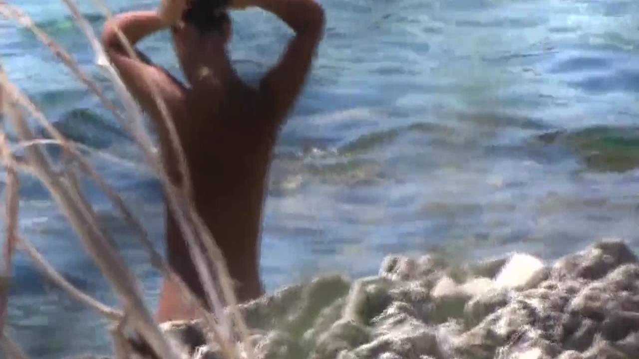 Jolie brune aux petits seins filmée sur une plage naturiste